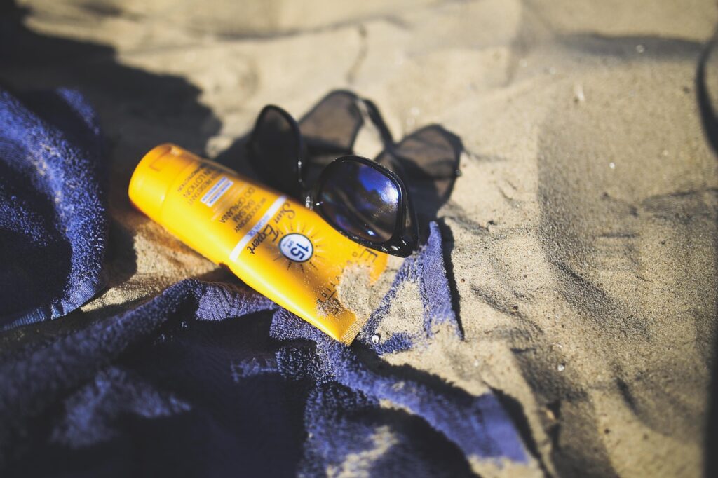 Crème solaire sur le sable avec une serviette et des lunettes soleil